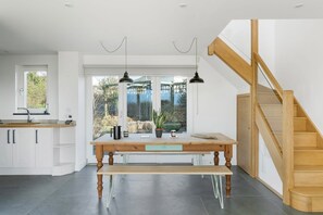 A modern kitchen with a large window, wooden staircase, and a bench.