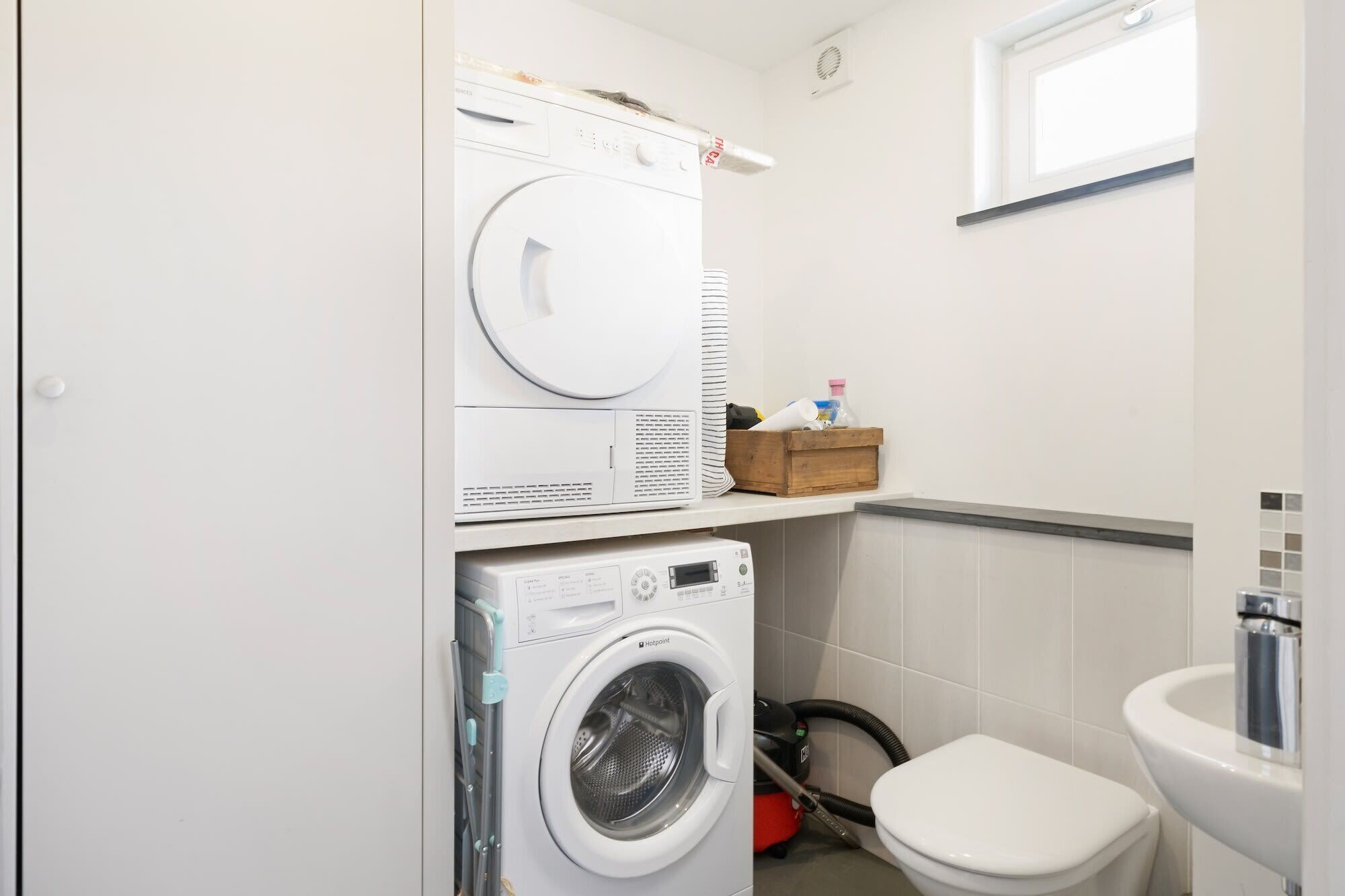 Ein kleiner Waschbereich mit einer Frontlader-Waschmaschine, einem übereinander angeordneten Trockner und einer Toilette.