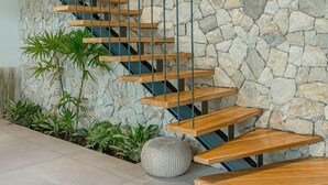 Una escalera moderna con escalones de madera y barandillas de metal, frente a una pared de piedra con textura.