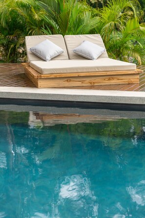 Relax in a serene outdoor space with a lounge area and pool surrounded by lush greenery.