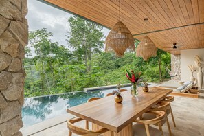 Enjoy al fresco dining in a serene setting with a table for four, pendant light, and lush green surroundings.