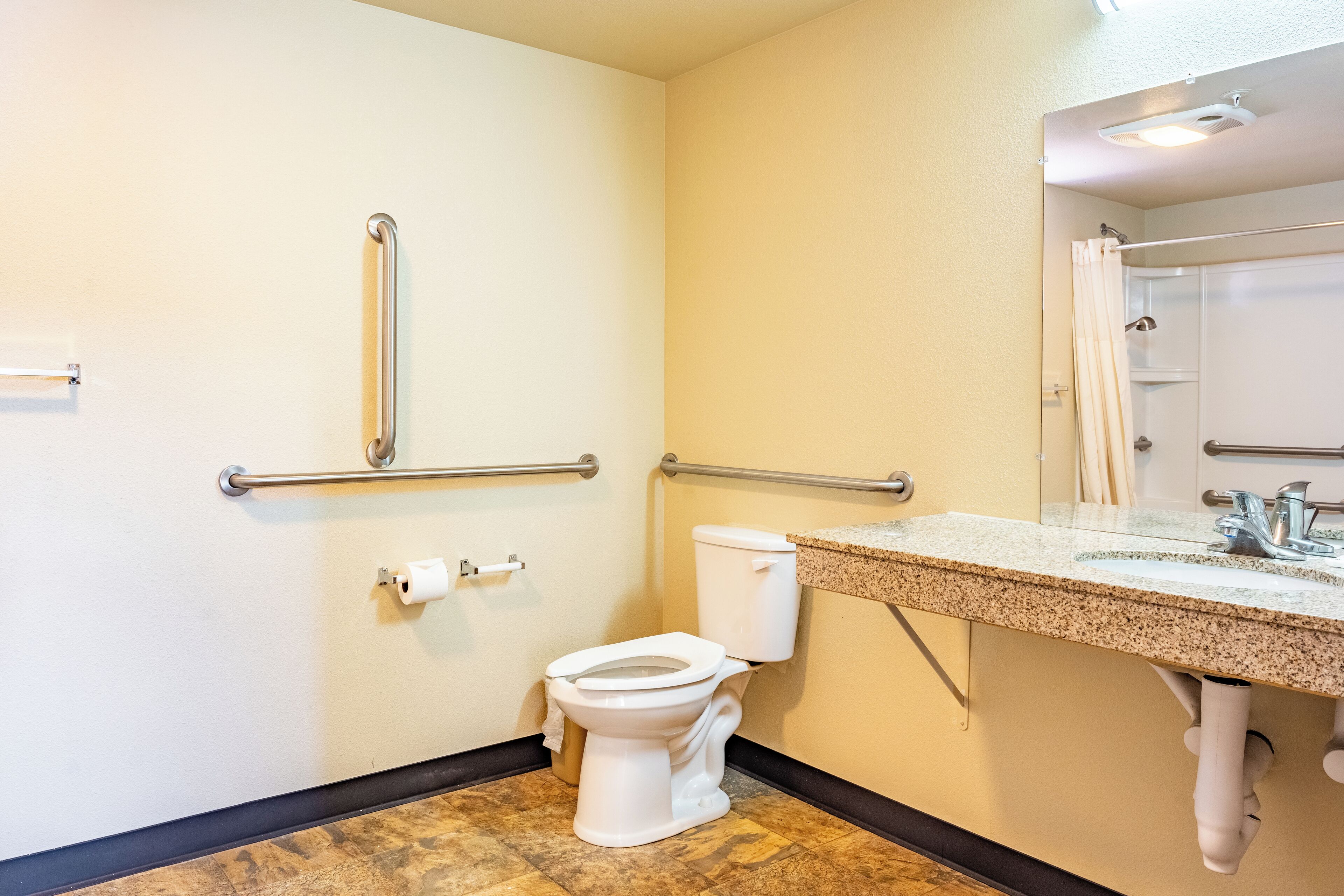 A bathroom with a toilet, grab bars, a sink, and a mirror.