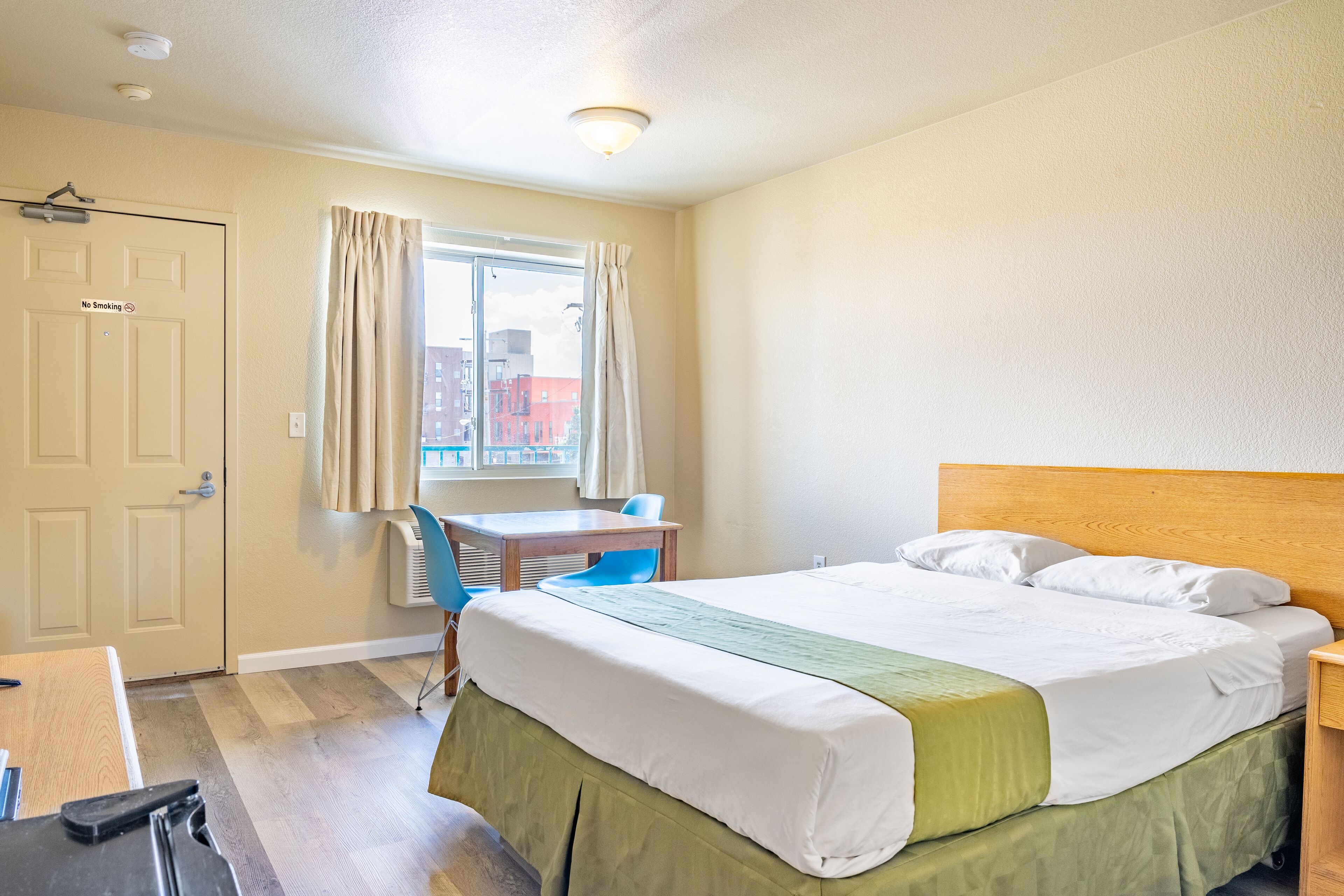 Une chambre d’hôtel avec un lit, un bureau, une chaise et une fenêtre avec des rideaux.