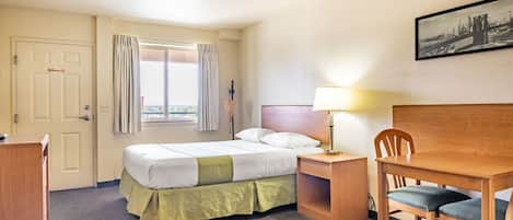 A hotel room with a bed, a desk, a chair, a lamp, and a window with curtains.