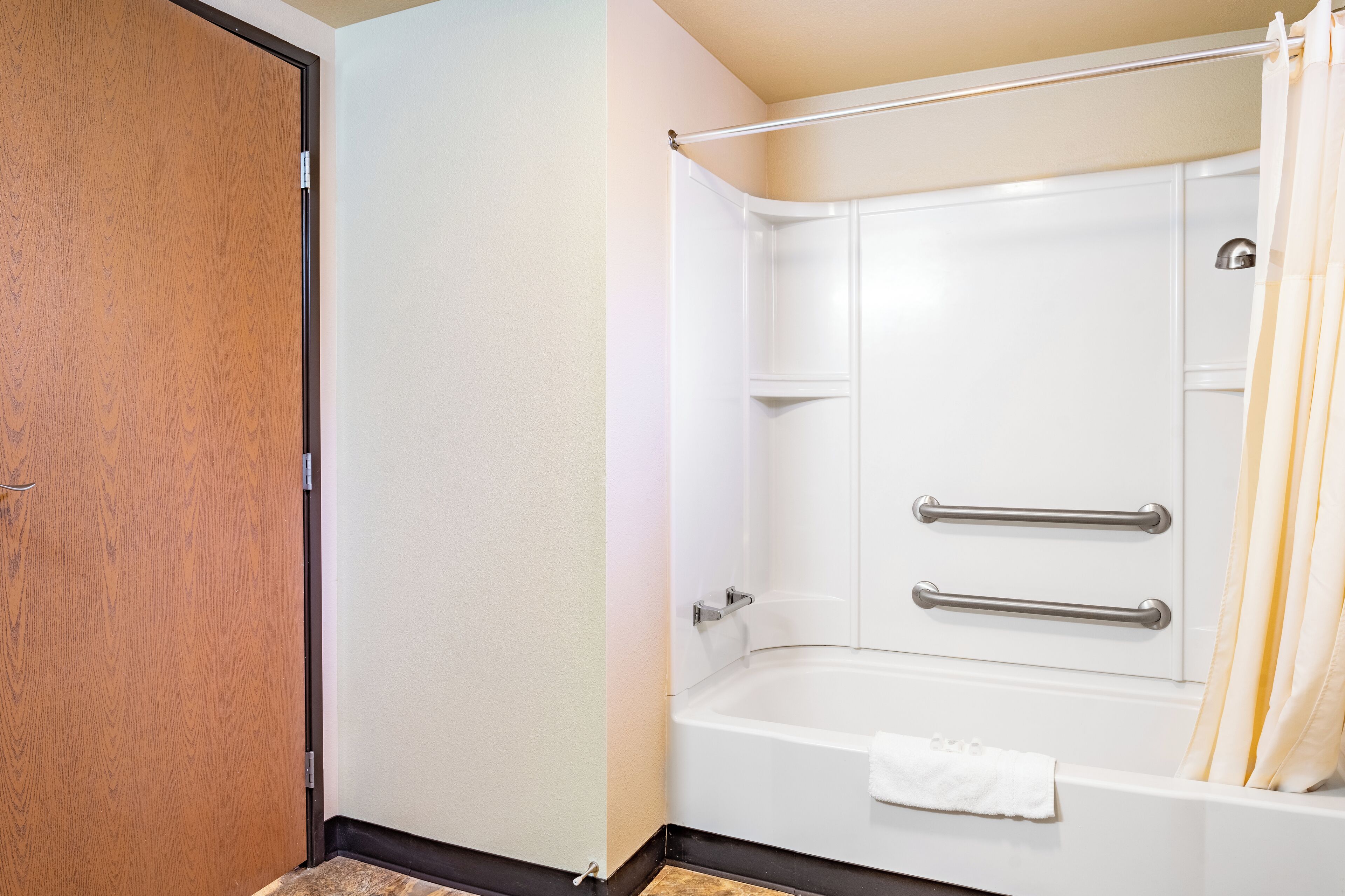 Un baño con puerta de madera, una bañera blanca con barras de apoyo y cortina de ducha.