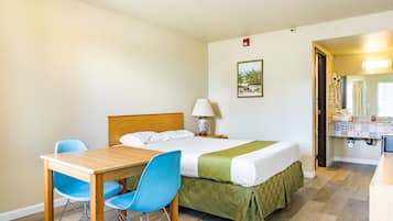 Una camera d'albergo con un letto, una scrivania con sedie, una lampada e un quadro appeso al muro.