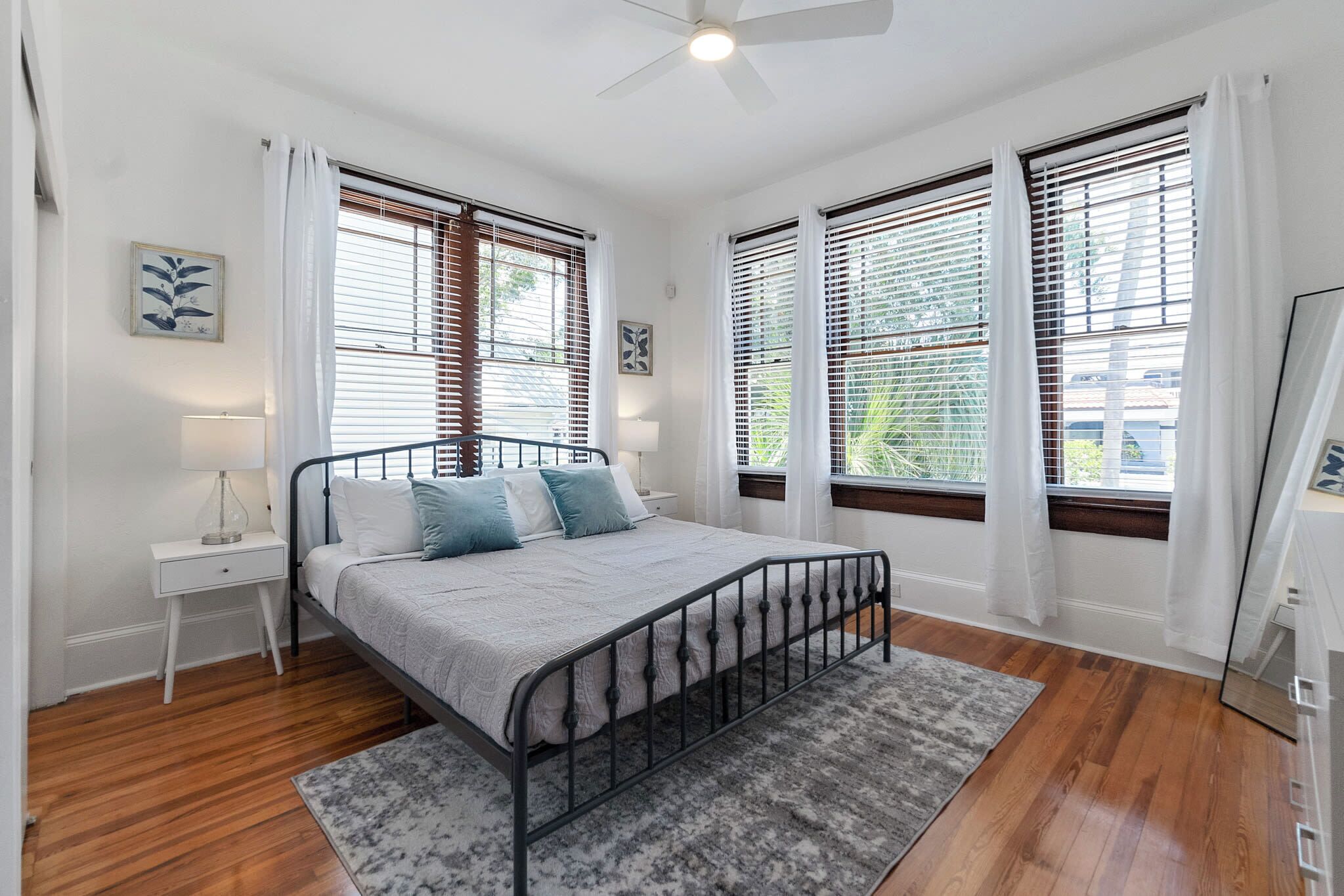 Quarto com cama, mesa de cabeceira, abajur e vista pela janela.