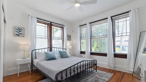 Un dormitorio con cama, mesita de noche, lámpara y vistas al exterior.