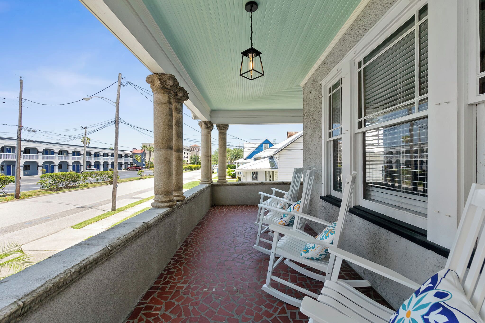 A covered porch with white rocking chairs and a tiled floor.