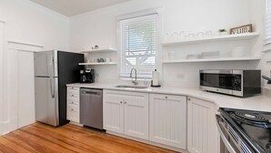Una cocina moderna con armarios blancos, un refrigerador de acero inoxidable, un lavavajillas, un microondas y una estufa.