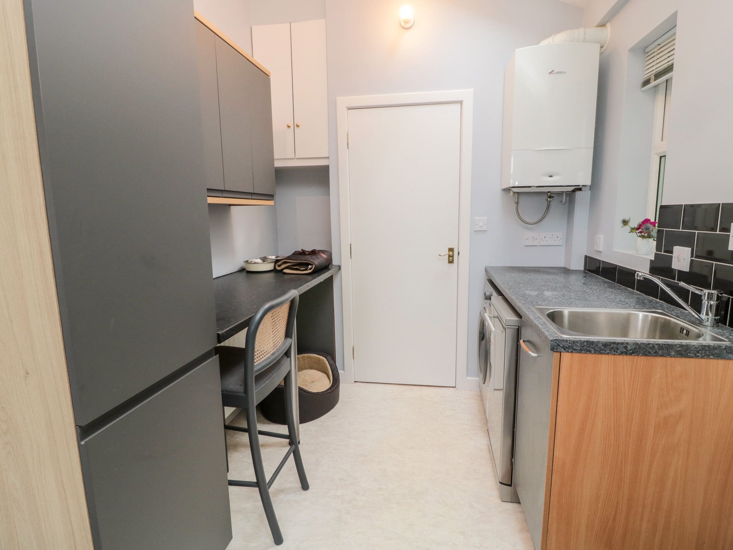 A compact kitchen with a dark countertop, a sink, and a small dining area with a chair.