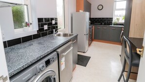 Een moderne keuken met een ingebouwde wasmachine, grijze kastjes en een zwart aanrecht.
