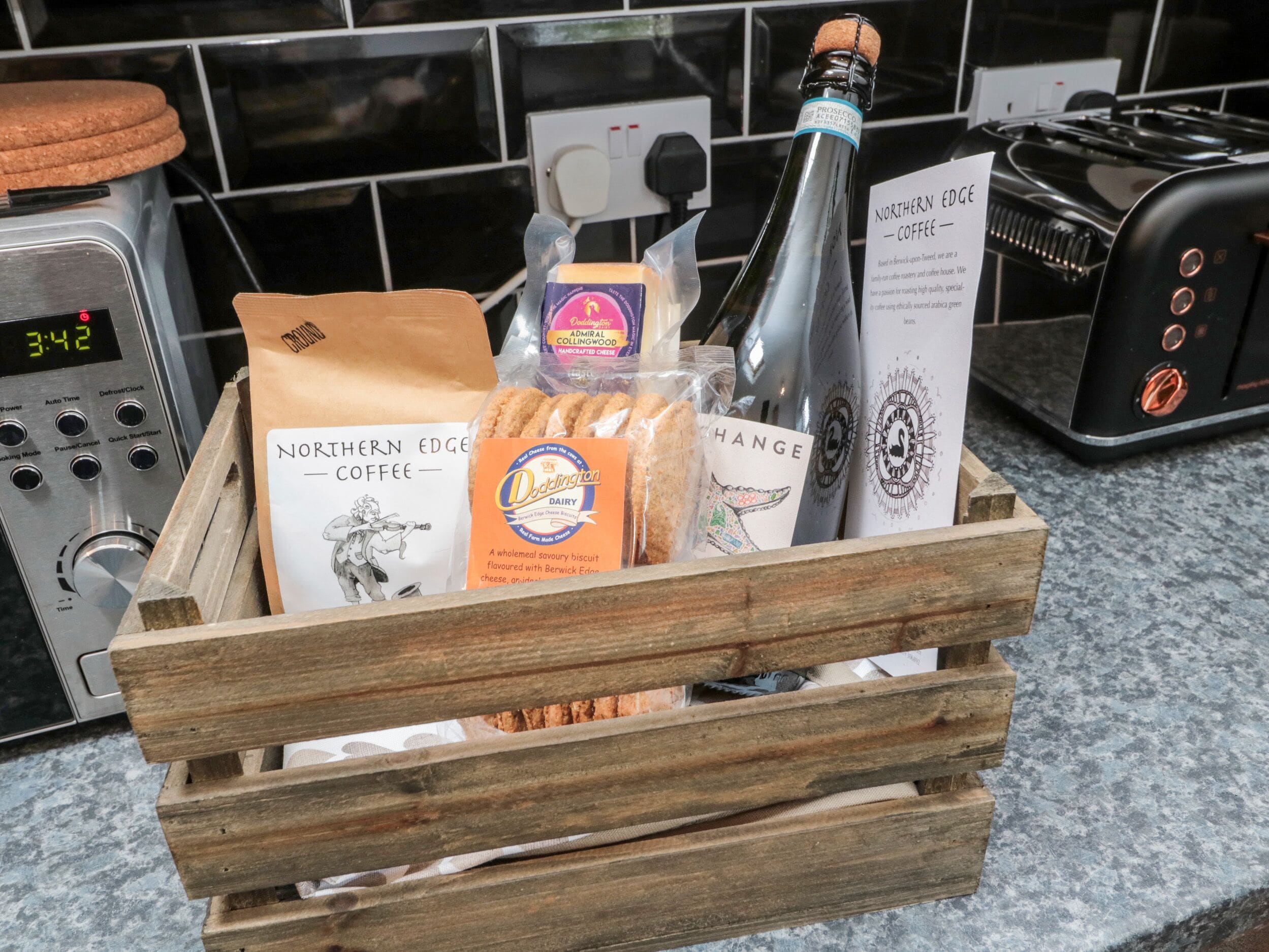 Una caja de madera con una botella de café Northern Edge, una galleta Doddington Dairy y un paquete de queso Admiral Collingwood.