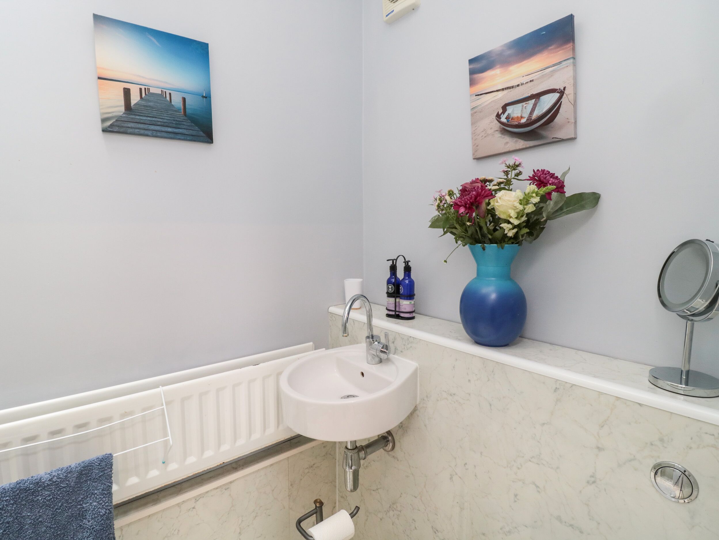 Ein Badezimmer mit einem weißen Waschbecken, einer blauen Vase mit Blumen und zwei gerahmten Bildern an der Wand.