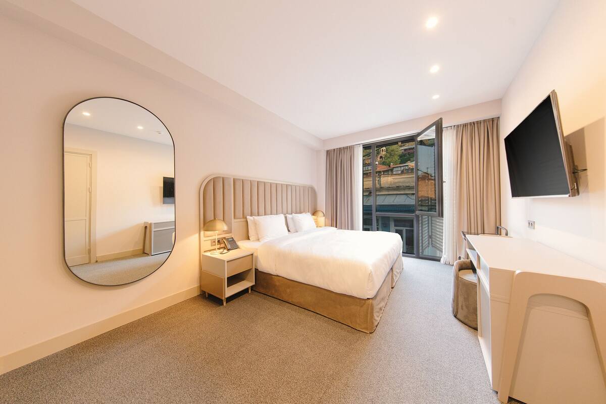 Una camera d'albergo moderna con un letto grande, comodini, una scrivania e un ampio specchio.