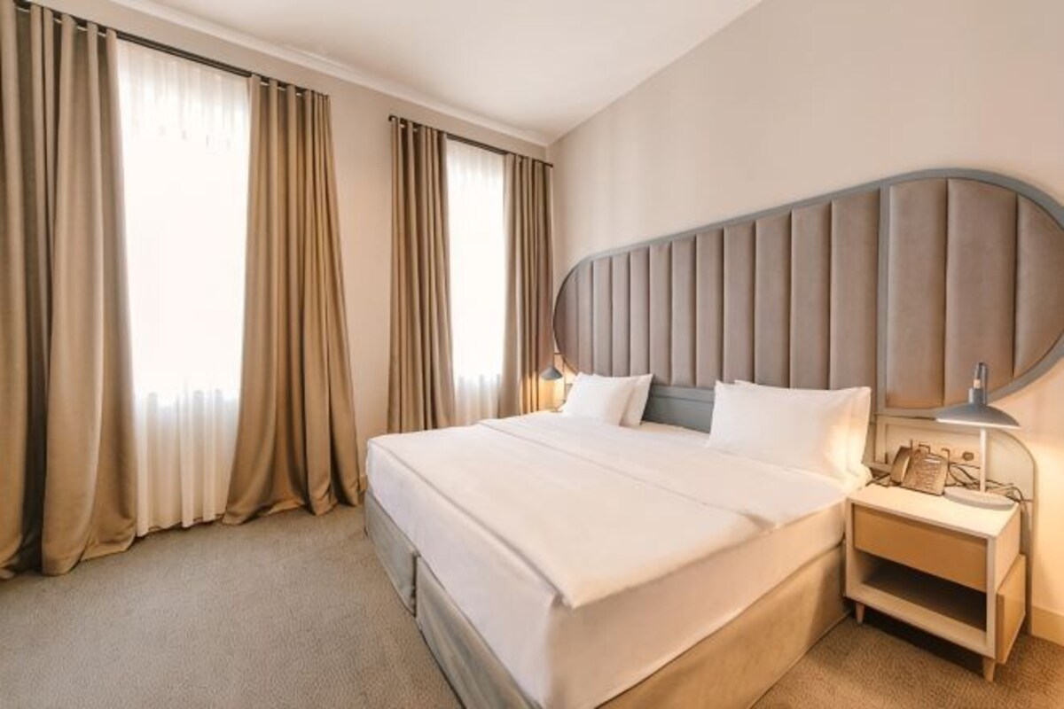 A hotel room with a large bed, a nightstand, a lamp, and curtains.