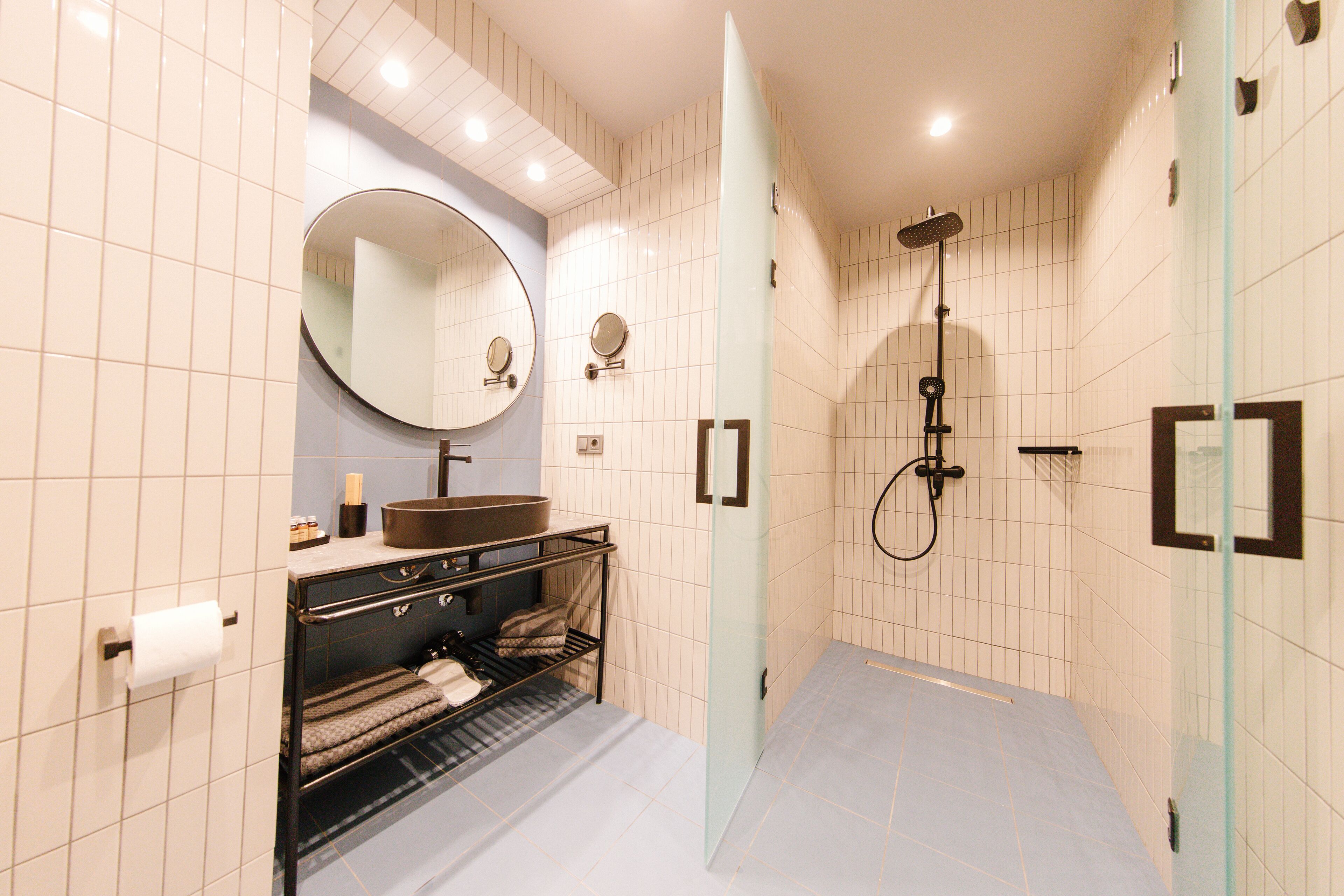 A modern bathroom with a glass shower enclosure, a round mirror, and a built-in sink.