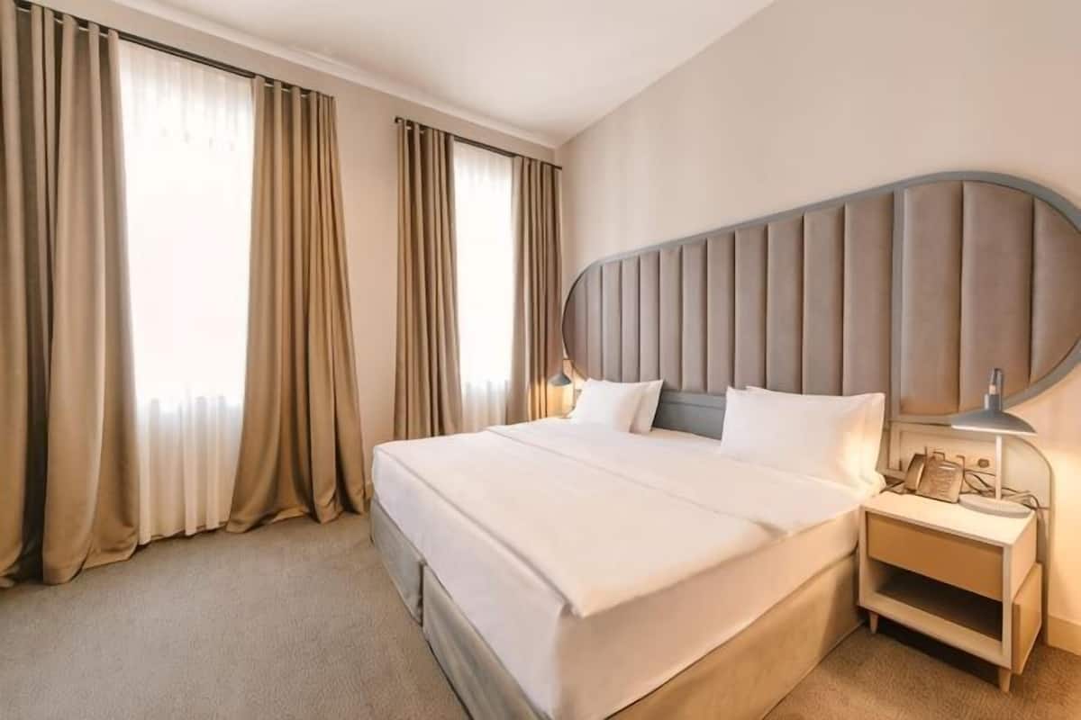 Una camera d'albergo con un letto grande, un comodino, una lampada e tende.