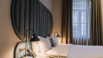 A hotel room with a bed, bedside lamps, a telephone, and a window with curtains.