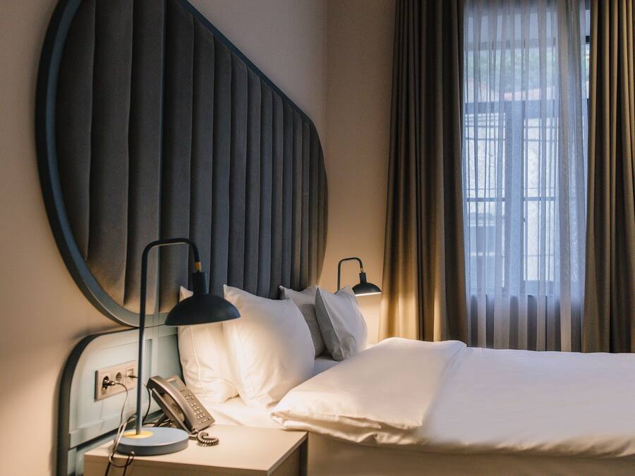 A hotel room with a bed, bedside lamps, a telephone, and a window with curtains.