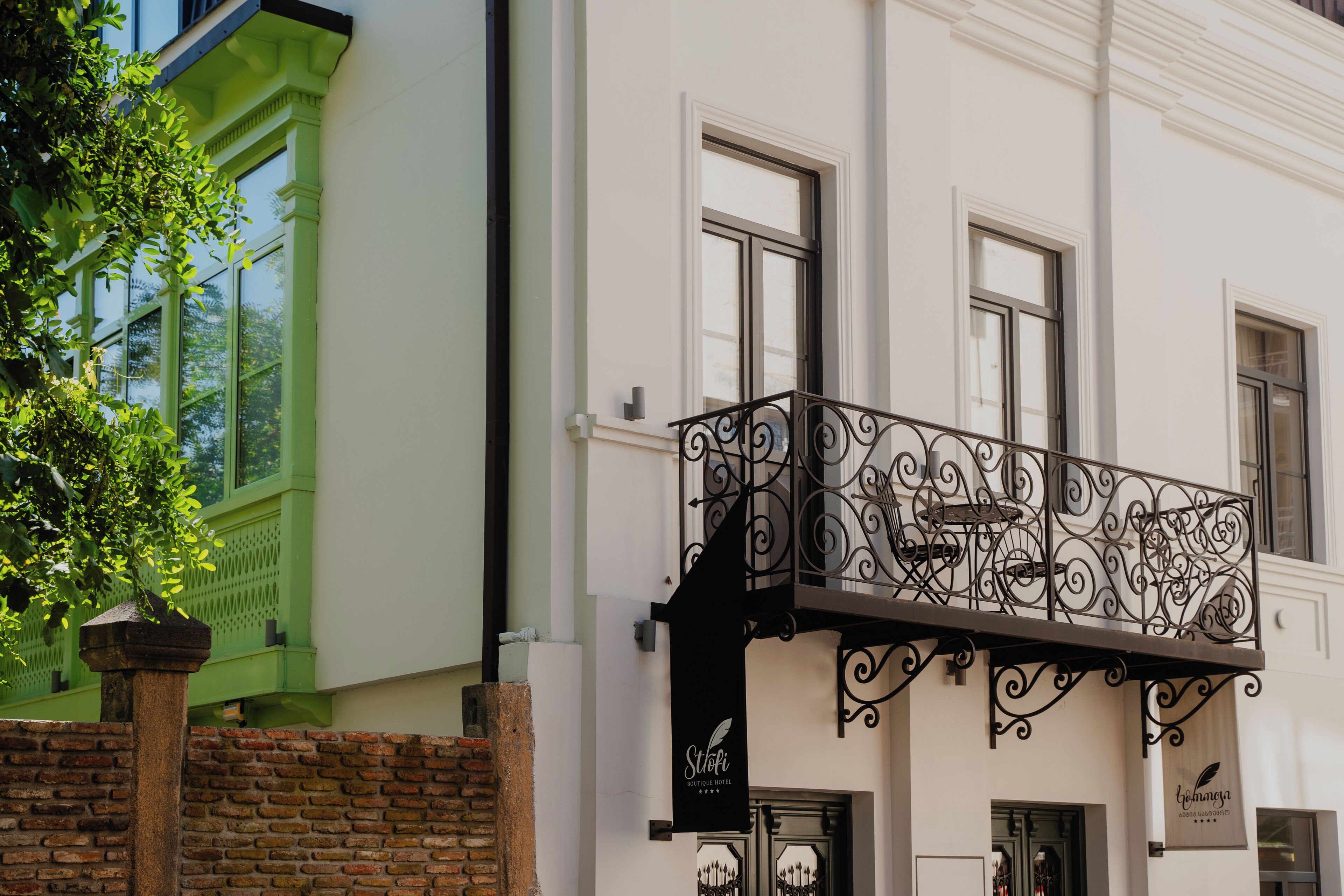 A building with a balcony featuring wrought iron railings, a brick wall, and a green window frame.