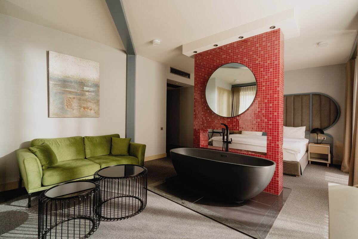 Un bagno moderno con una vasca freestanding nera, un divano verde e uno specchio rotondo.
