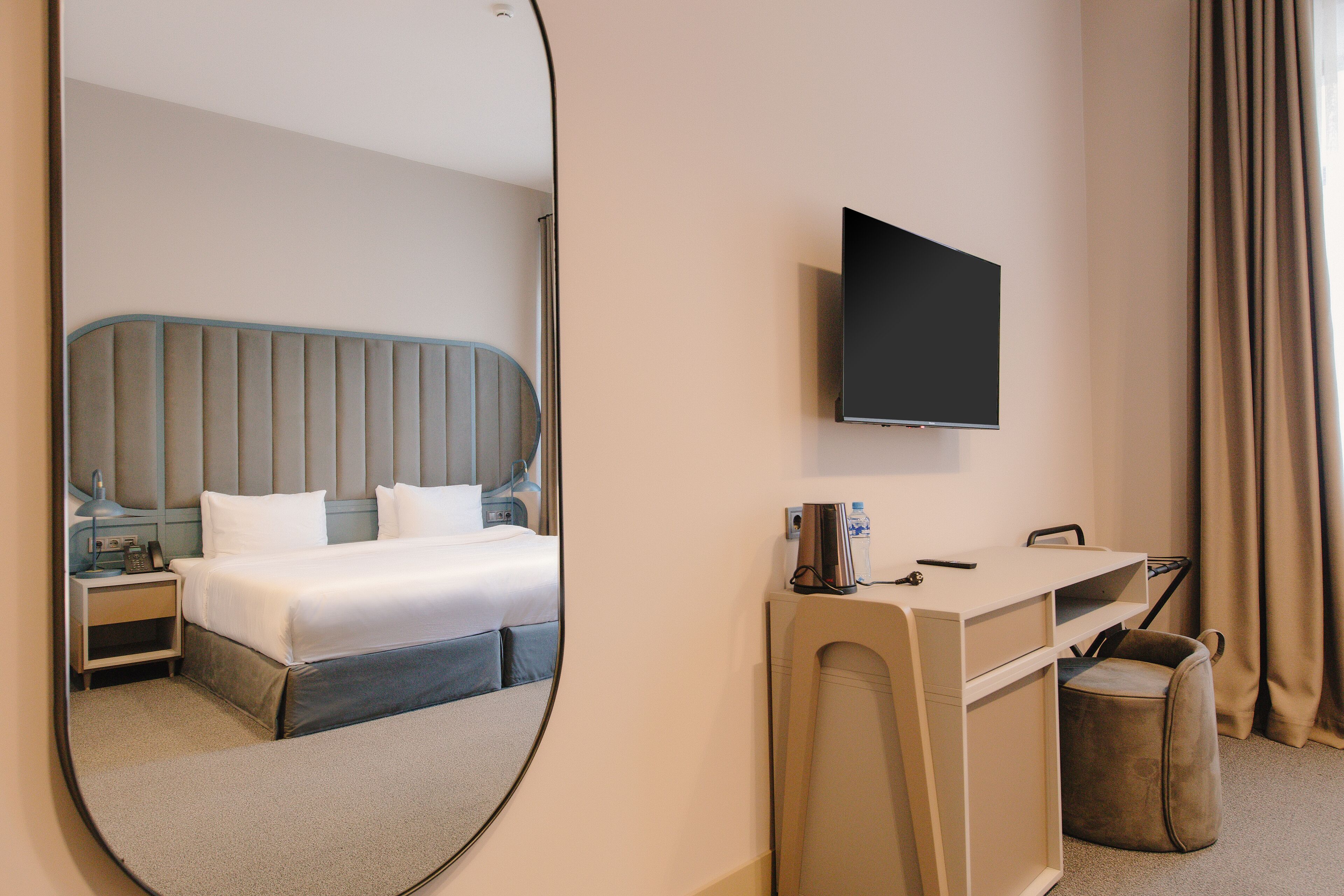 A hotel room with a bed, a desk, a TV, and a mirror.