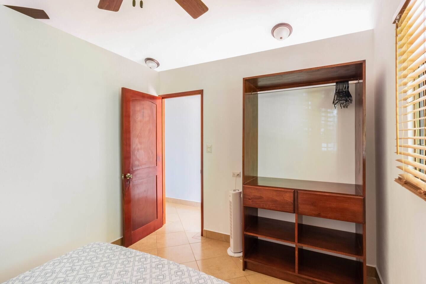 Une chambre à coucher comprenant un lit, une armoire, un ventilateur de plafond et une fenêtre avec des stores.