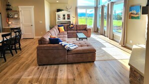 A spacious living room with a large brown sectional sofa, a dining area with a table and chairs, and a kitchen in the background. - New home in the heart of Alpine! (Alpine)