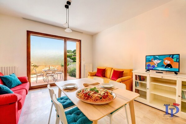 A dining area with a table set for two, a sofa, and a television on a cabinet.
