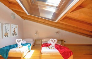 A cozy attic bedroom with two beds, wooden beams, skylight, and wall art.