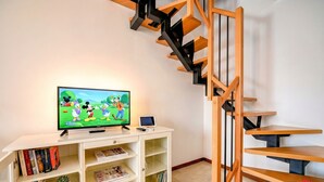 Een woonkamer met een flatscreen televisie, boekenkasten, een klein plantje en een houten trap.