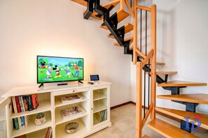 A living room with a flat-screen TV, bookshelves, a small plant, and a wooden staircase.