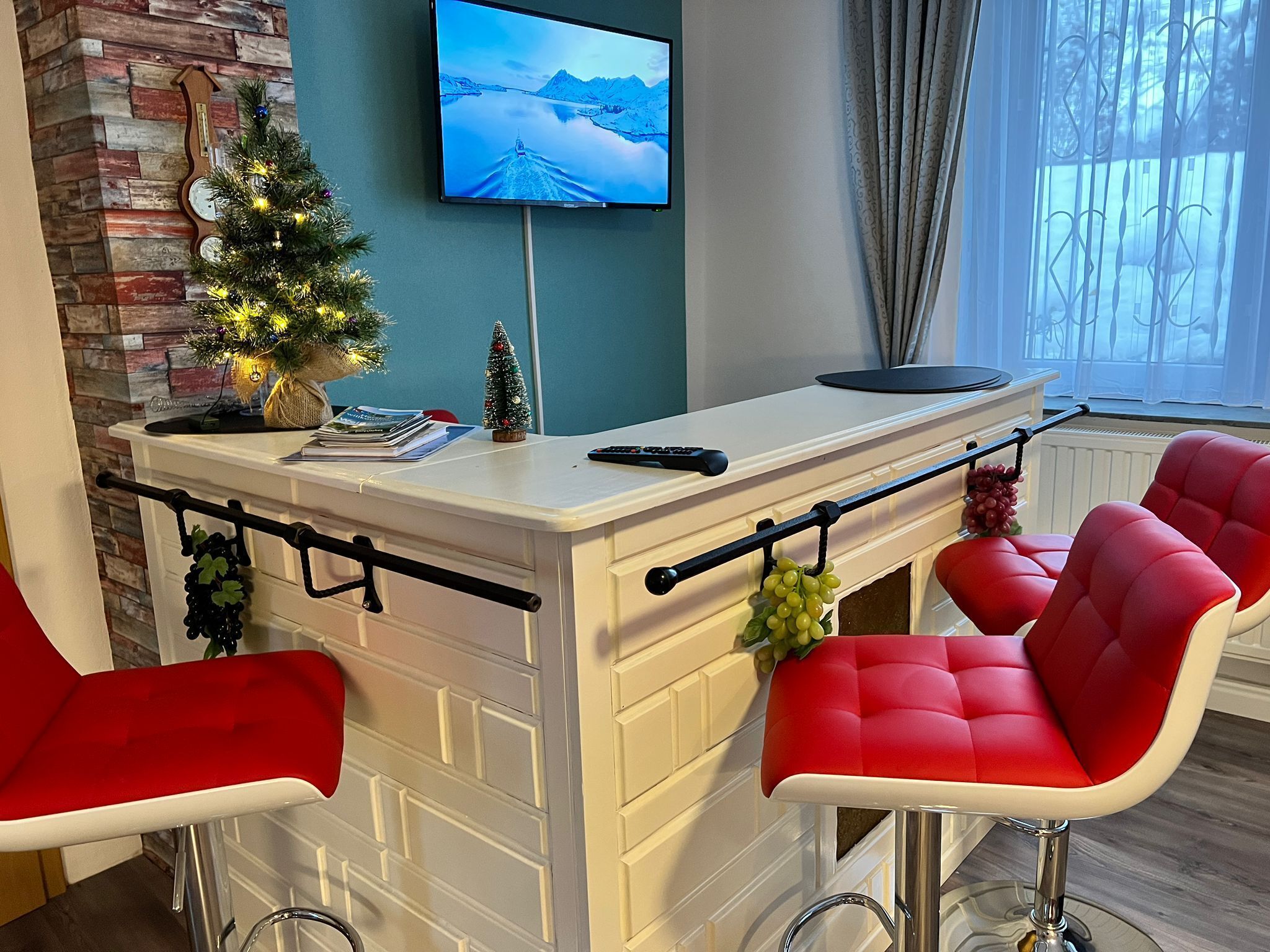 A modern kitchen with a white countertop, red bar stools, a small Christmas tree, and a TV mounted on the wall.