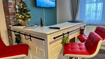 A modern kitchen with a white countertop, red bar stools, a small Christmas tree, and a TV mounted on the wall.