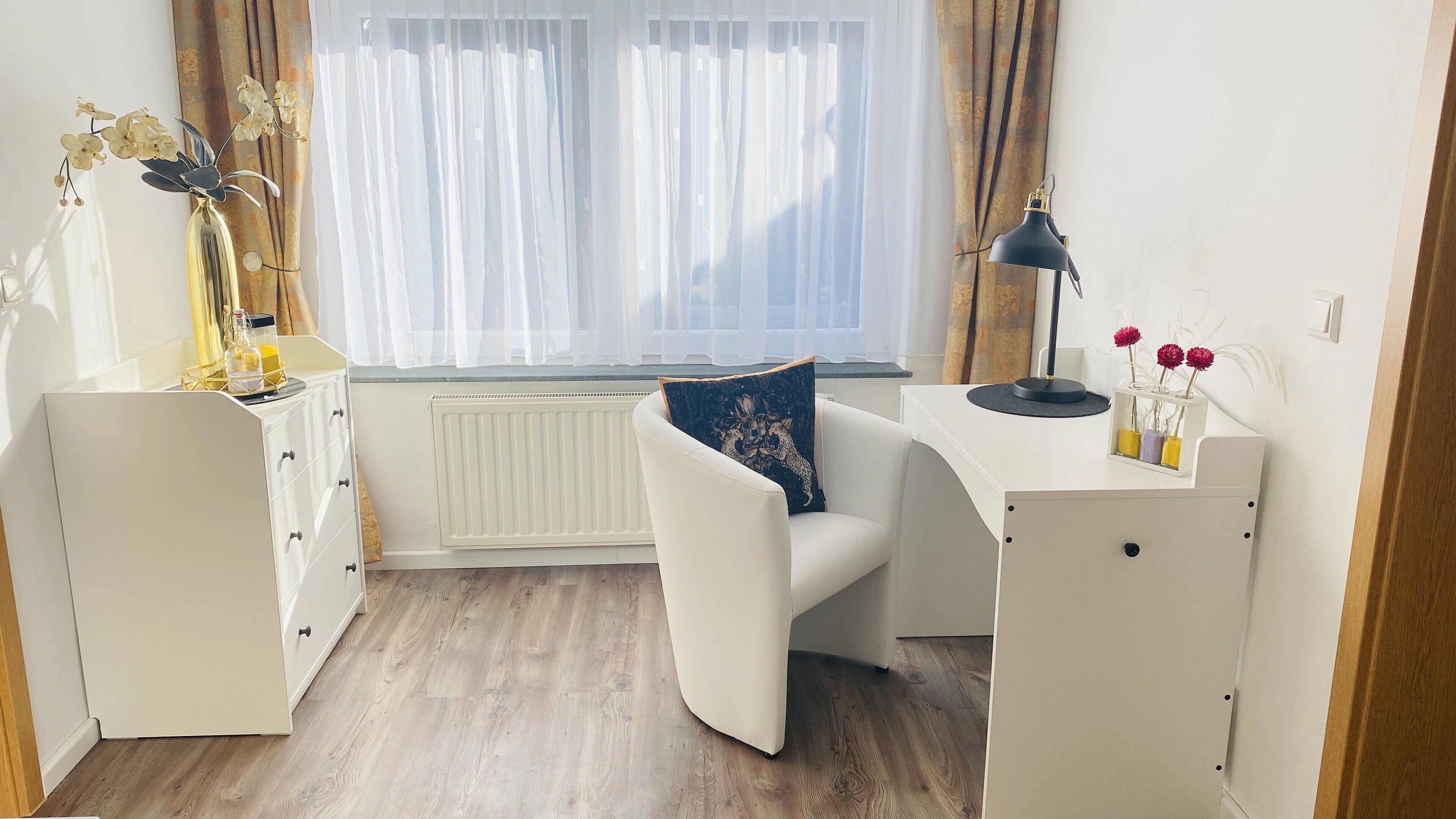 A modern, well-lit room with a white desk, a comfortable chair, and a radiator.