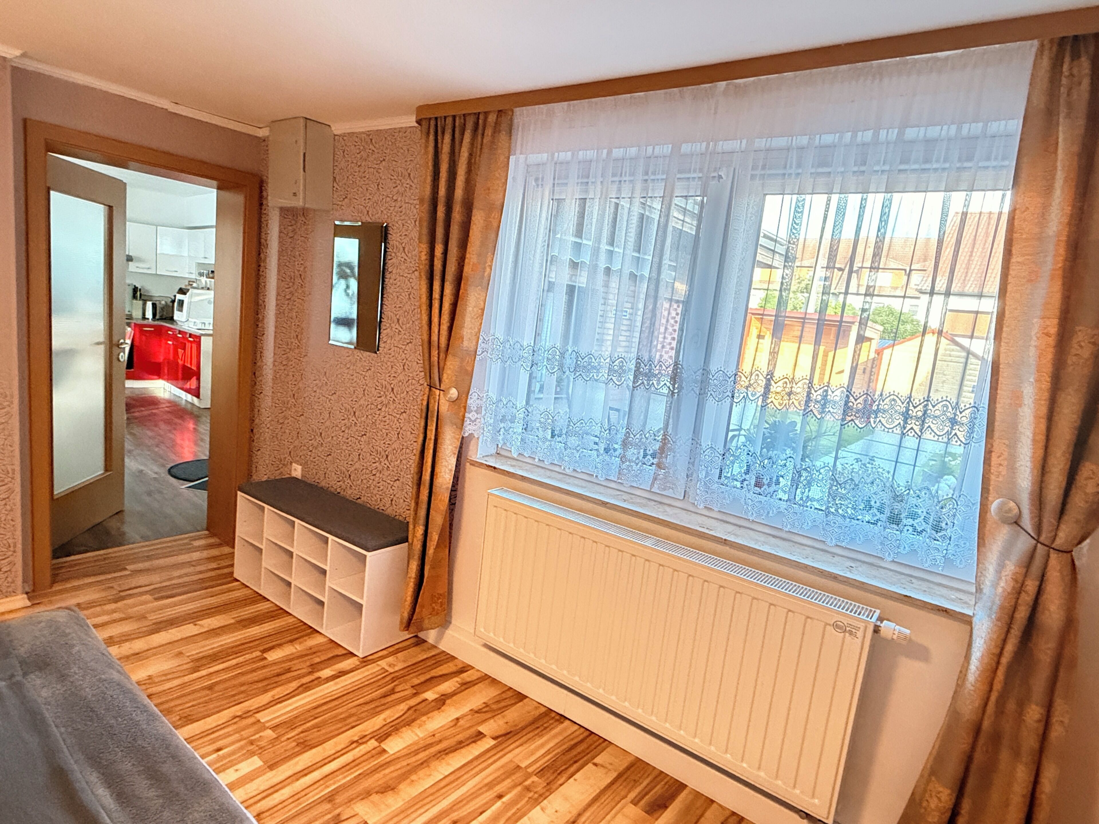 Une pièce avec un plancher en bois, un banc, un radiateur et une fenêtre avec des rideaux.