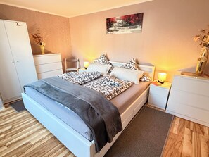 A bedroom with a bed, bedside tables, a nightstand, a wardrobe, and a painting on the wall. - Modern 4-star apartment - stylish comfort, relaxation for people and dogs! (Weißenfels)