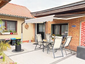 A patio with a table and chairs, a trash bin, and potted plants. - Modern 4-star apartment - stylish comfort, relaxation for people and dogs! (Weißenfels)