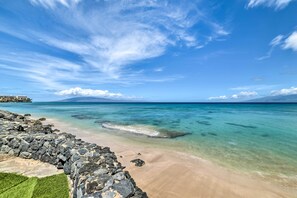 A beach with clear turquoise water, a rocky shoreline, and a distant mountain. - Beachfront Condo: Sunset Views & Pool Access! (Lahaina)