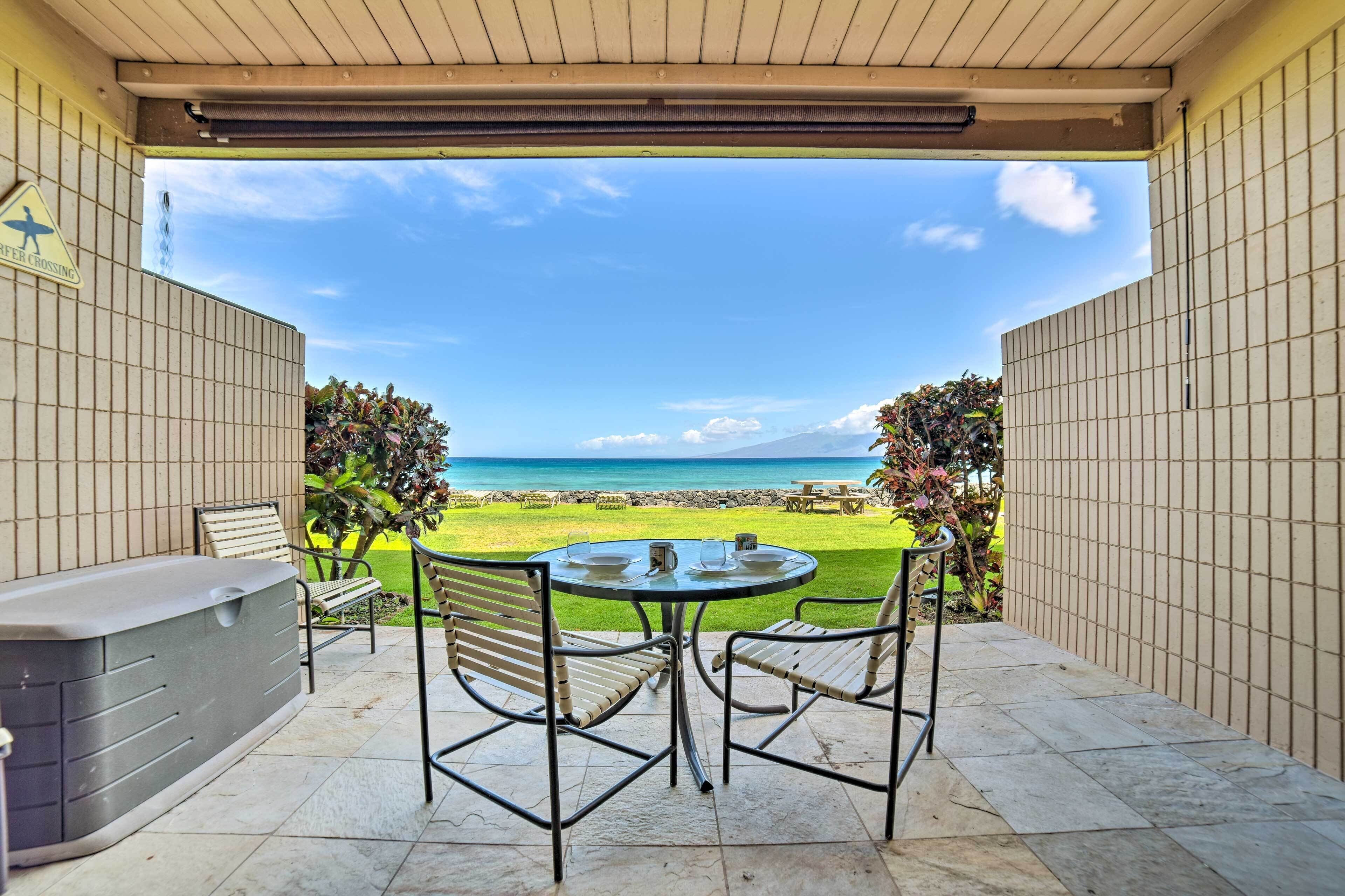 A covered patio with a table and chairs, a hot tub, and a view of the beach and ocean.
