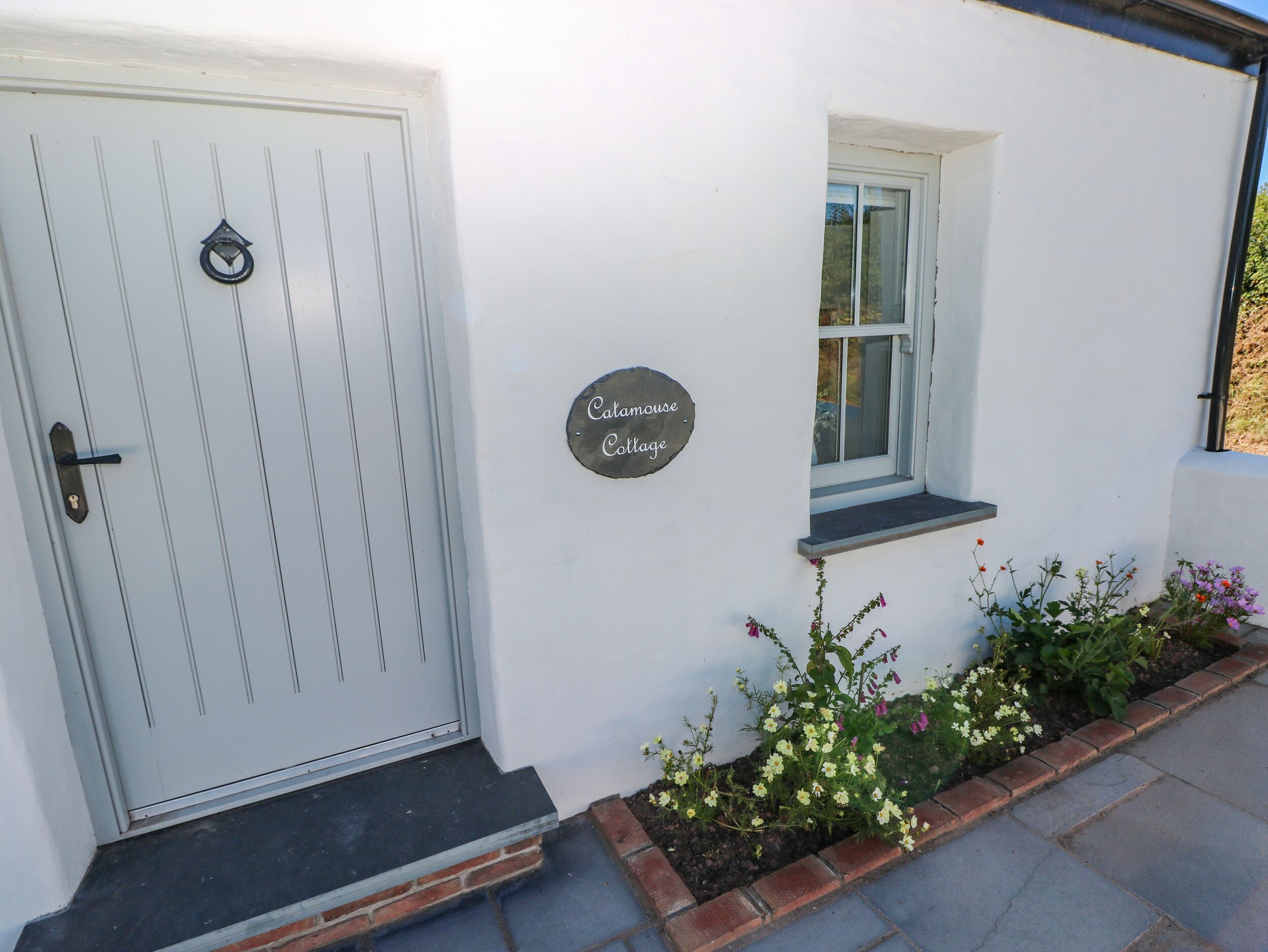 A white cottage with a door, a window, and a sign that reads "Catamouse Cottage".