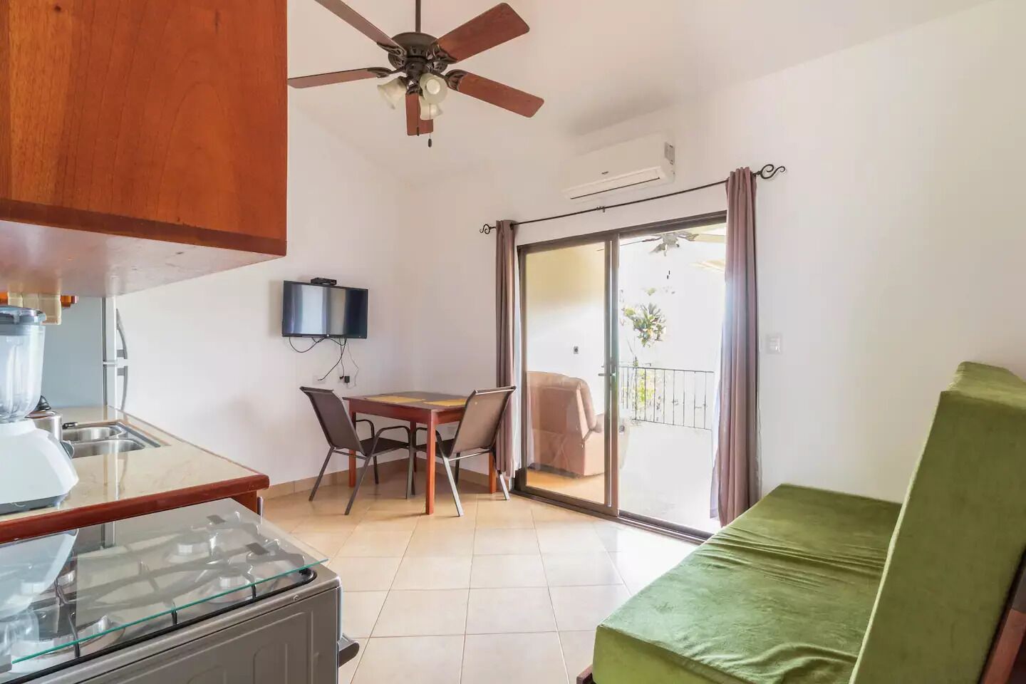 Un ambiente compatto con angolo cottura, zona pranzo, divano verde e balcone con vista.