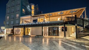Un hotel moderno con un llamativo letrero de "Harbor Hotel & Casino", que cuenta con una entrada espaciosa, un área exterior cubierta y una escalera que conduce a los pisos superiores.