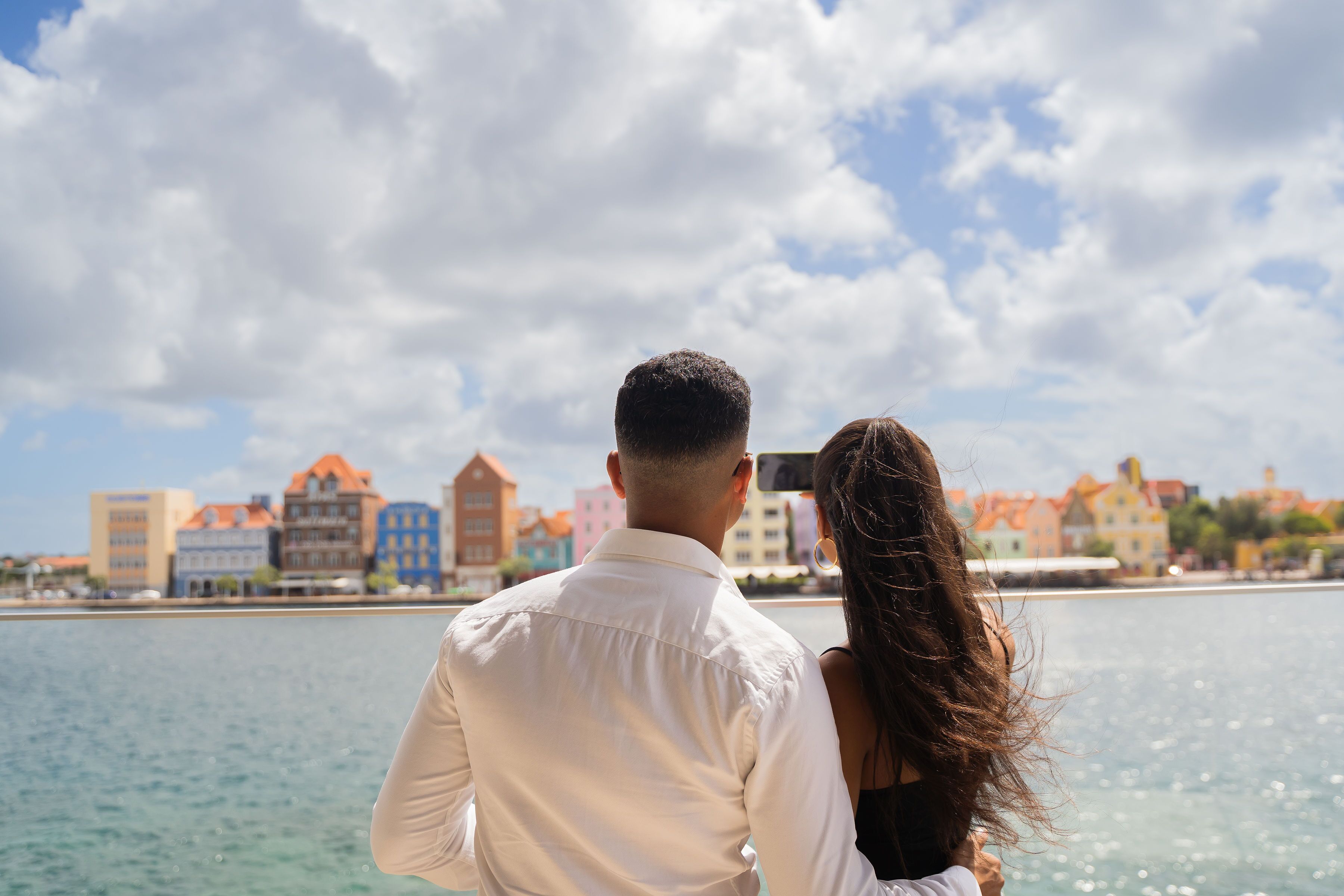 A couple overlooking a waterfront with buildings in the background.