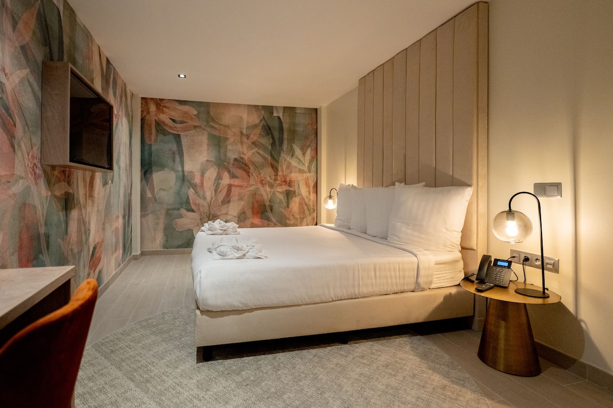 Una habitación de hotel moderna con una cama grande, una mesita de noche con teléfono y un televisor montado en la pared.