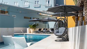 Una piscina al aire libre, sombrillas, sillones reclinables de piscina