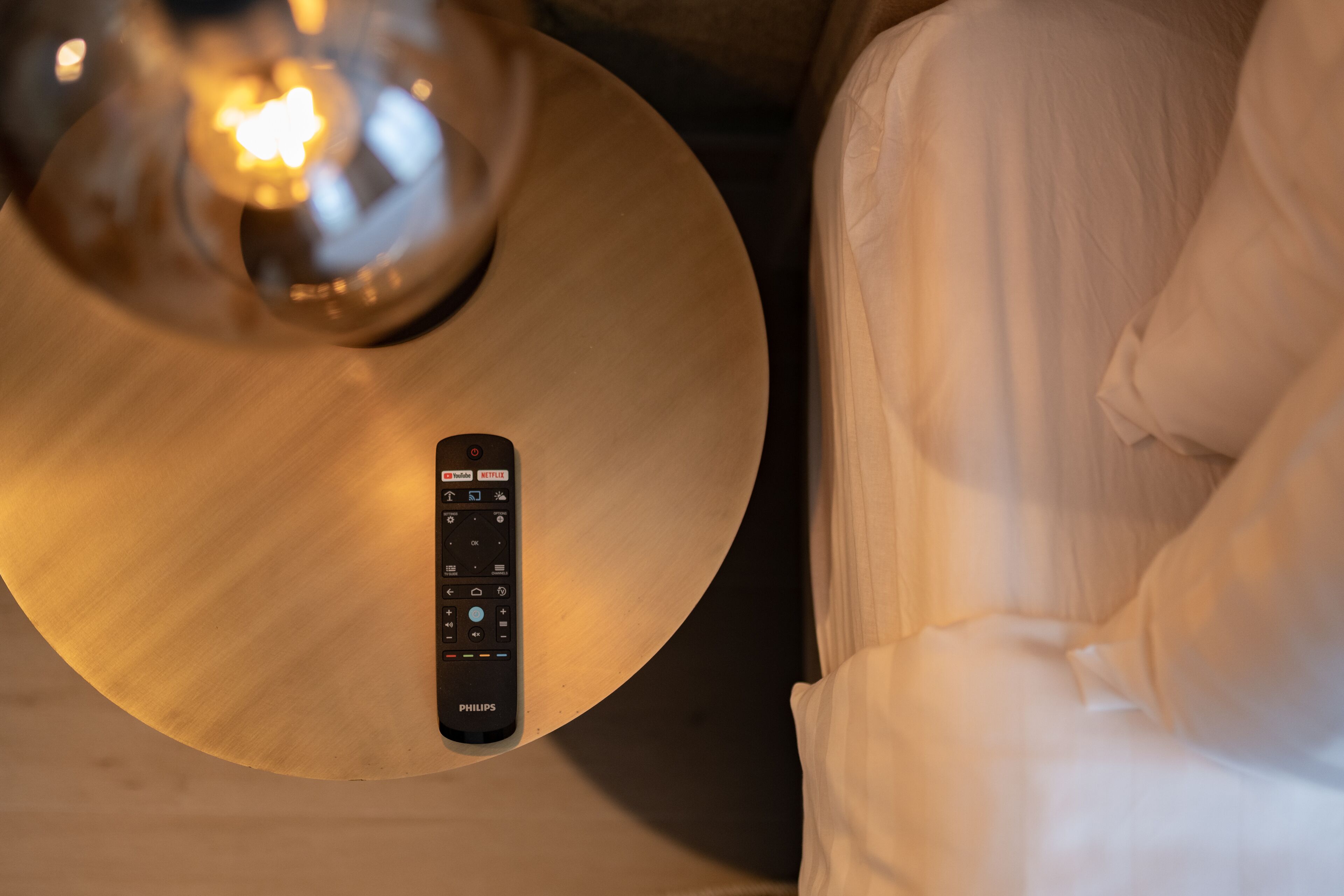 A remote control on a round table with a light fixture above it.