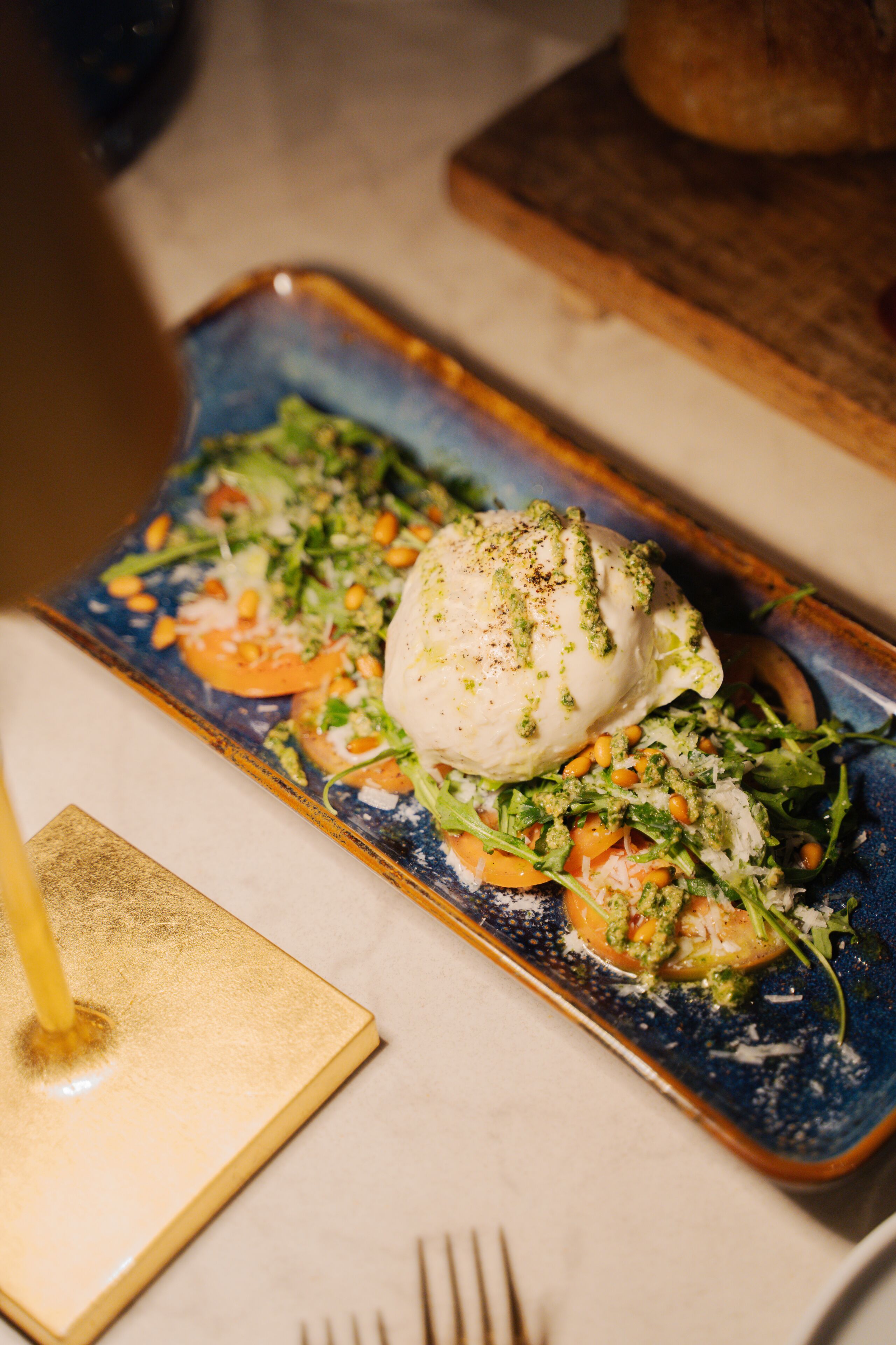 A rectangular plate with a poached egg on top, surrounded by greens, tomatoes, and a creamy sauce, served on a blue and gold patterned plate.