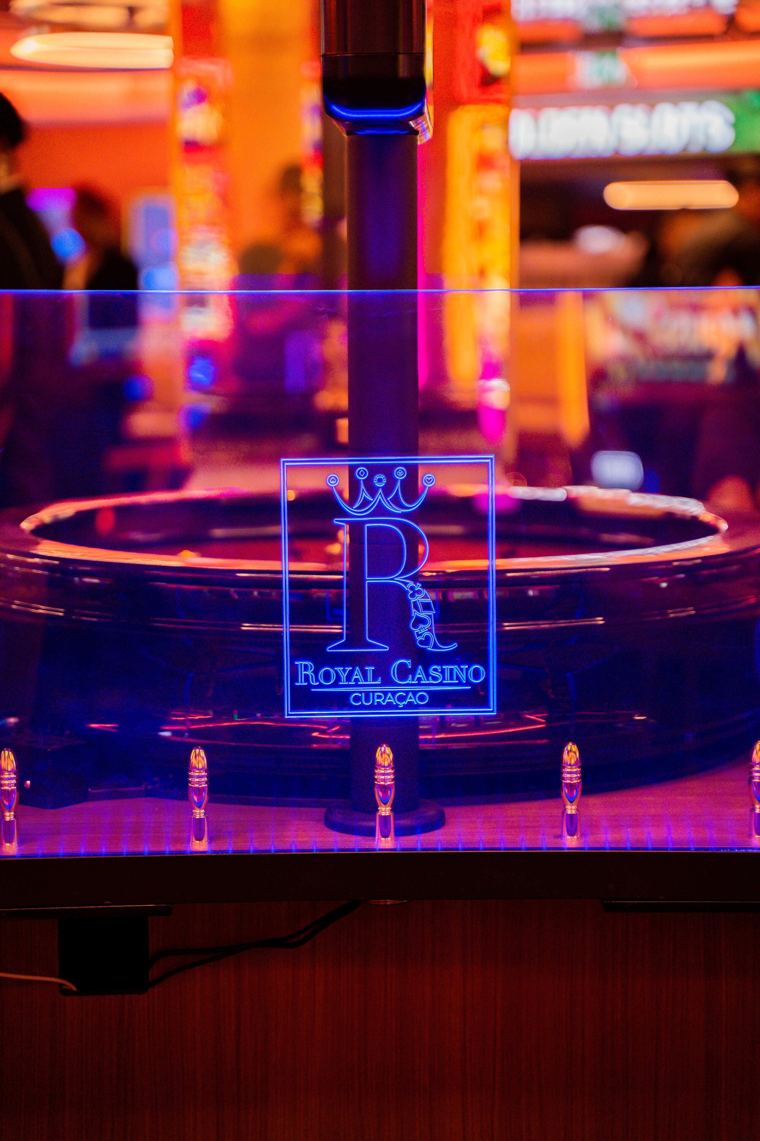 Ein Roulette-Tisch mit dem Schriftzug "Royal Casino“, umgeben von beleuchteten Glaspaneelen.